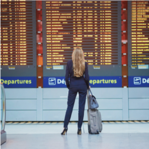 a woman with her luggage standing in front of a big airport flight board.